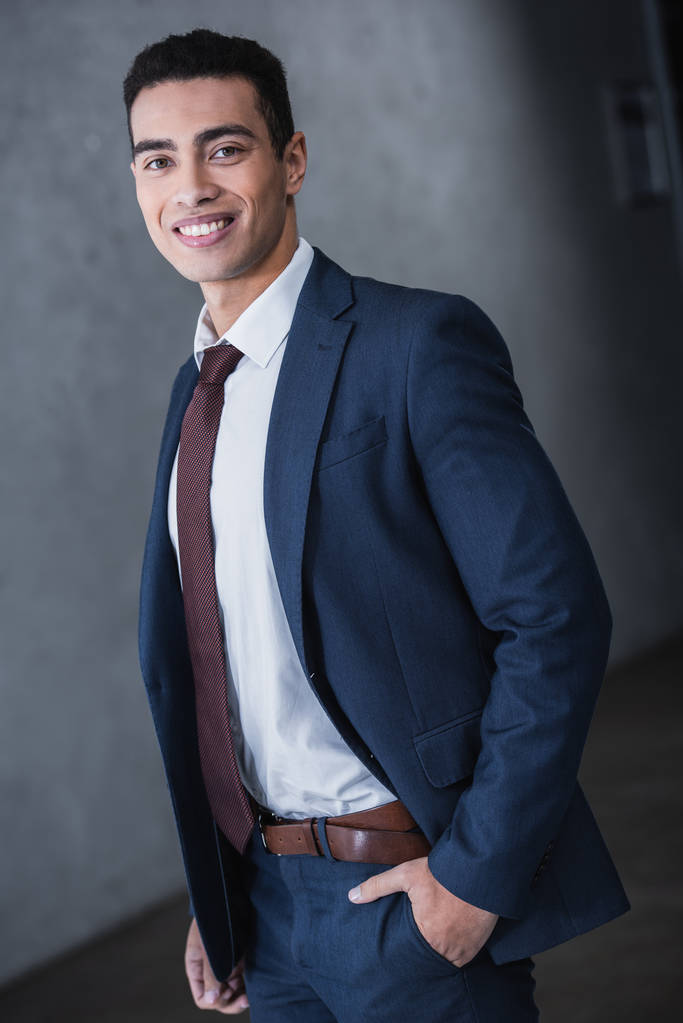 portrait of handsome young mixed race businessman standing with hand in pocket and smiling at camera - Photo, Image
