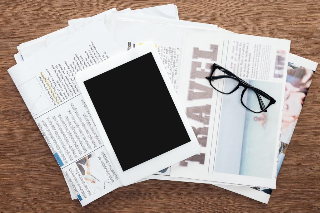 felülnézet-tabletta, üres képernyő, szemüveg és újságok-a fából készült asztallap - Fotó, kép