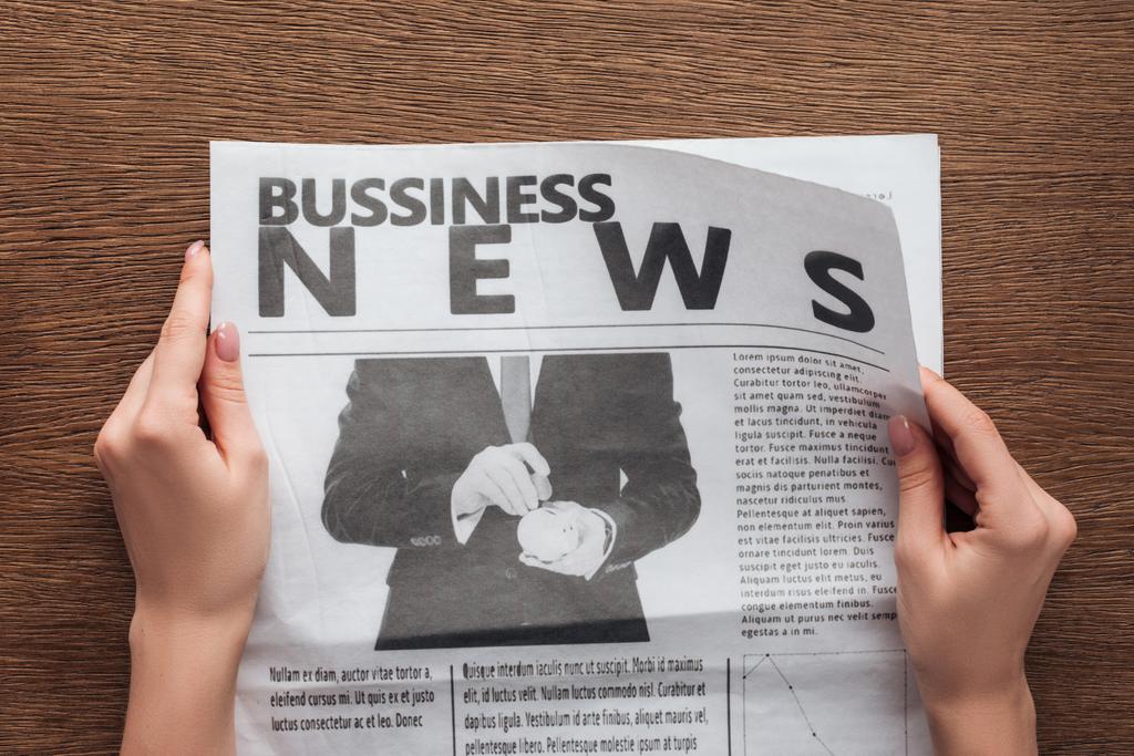 imagen recortada de periodista leyendo periódico de negocios en mesa de madera
 - Foto, Imagen