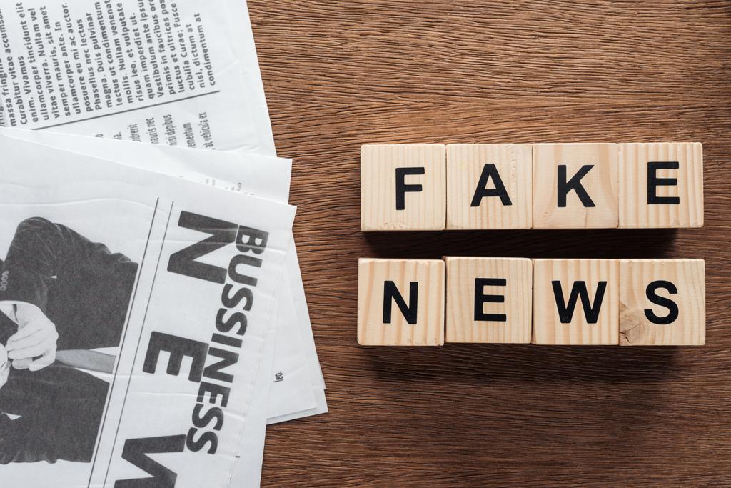 Ansicht von Holzwürfeln mit Wörtern Fake News und Zeitungen auf hölzerner Tischplatte - Foto, Bild