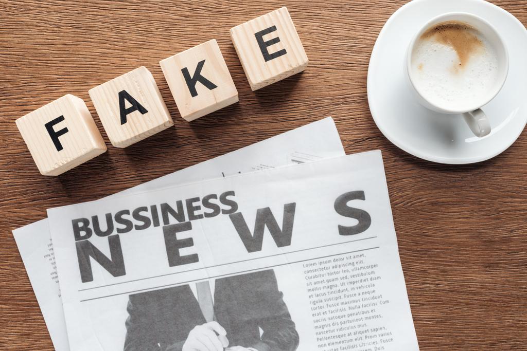 Κάτοψη των ξύλινων κύβων με λέξη fake, επιχειρηματική εφημερίδα και καφέ σε ξύλινη επιτραπέζια - Φωτογραφία, εικόνα