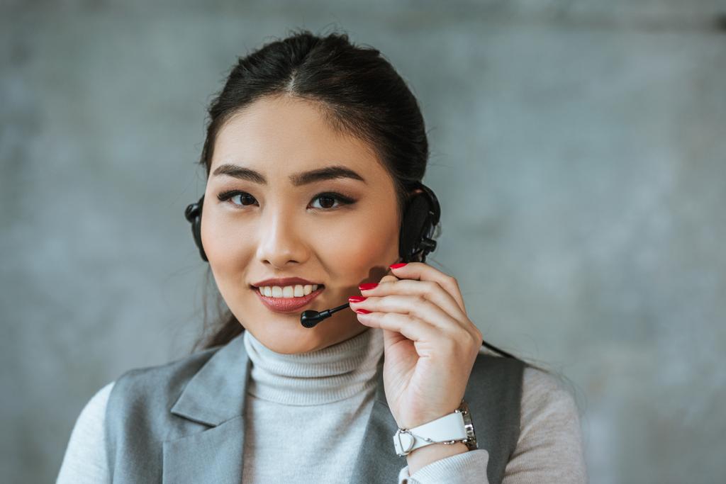 bela jovem asiático call center operador sorrindo para câmera no cinza
 - Foto, Imagem