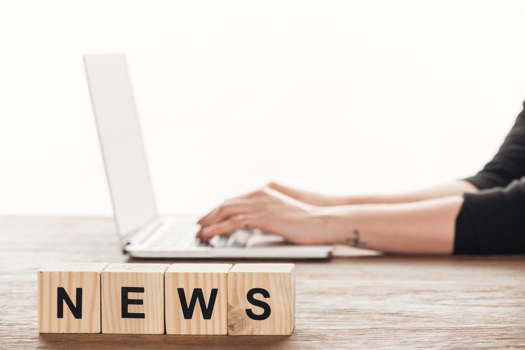 обрізане зображення журналіста, який працює на ноутбуці, дерев'яні кубики зі словом новини на стільниці
 - Фото, зображення