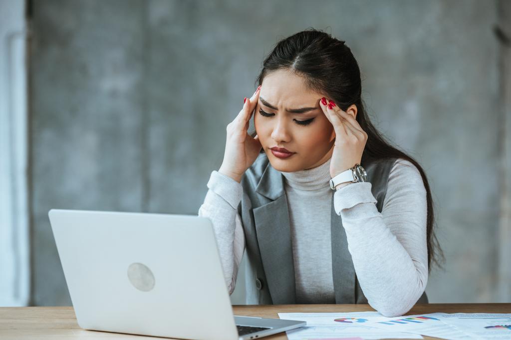gestresste junge Geschäftsfrau mit Kopfschmerzen bei der Arbeit mit Laptop im Büro - Foto, Bild