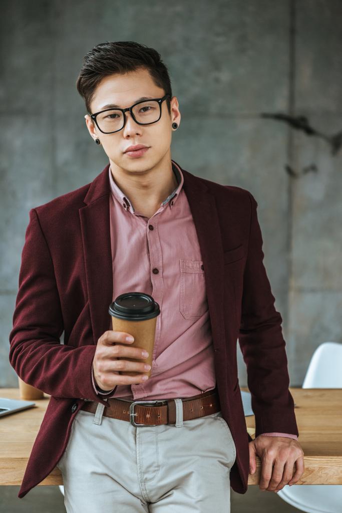 schöner junger asiatischer Mann mit Kaffee zu gehen und Blick auf die Kamera im Büro - Foto, Bild