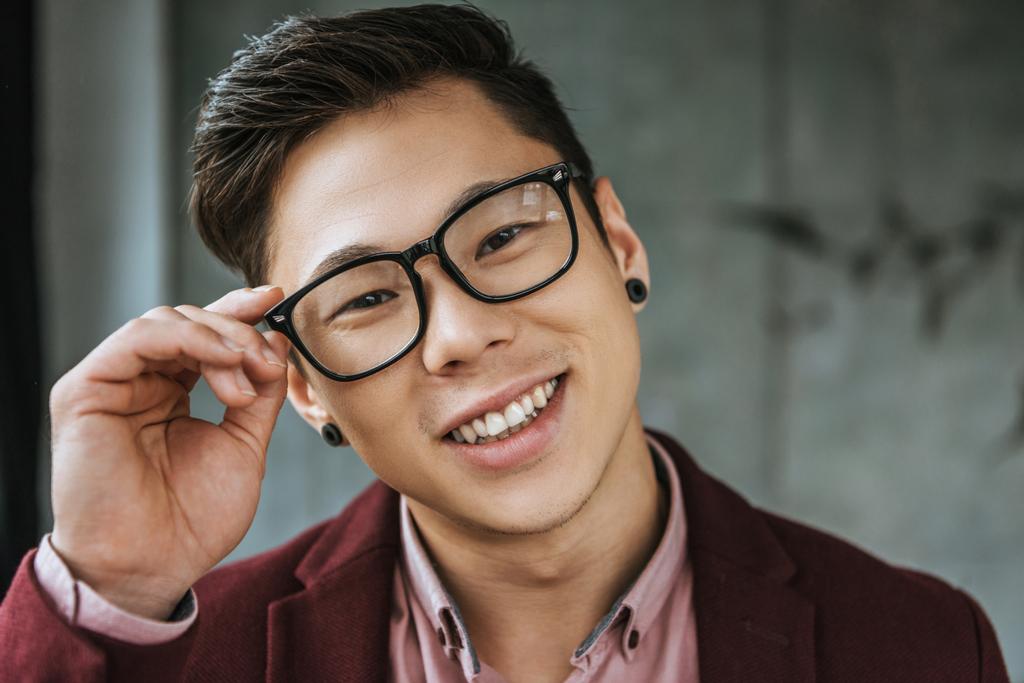 Porträt eines hübschen jungen asiatischen Mannes, der eine Brille einsetzt und in die Kamera lächelt - Foto, Bild