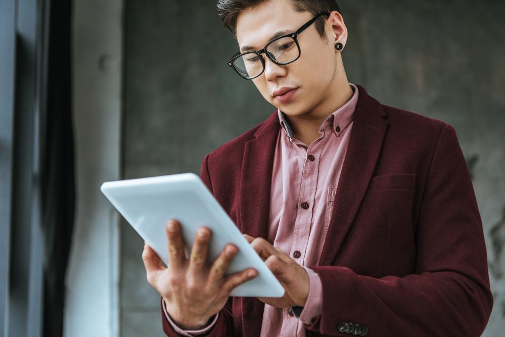 зосереджений молодий чоловік в окулярах, використовуючи цифровий планшет в офісі
  - Фото, зображення