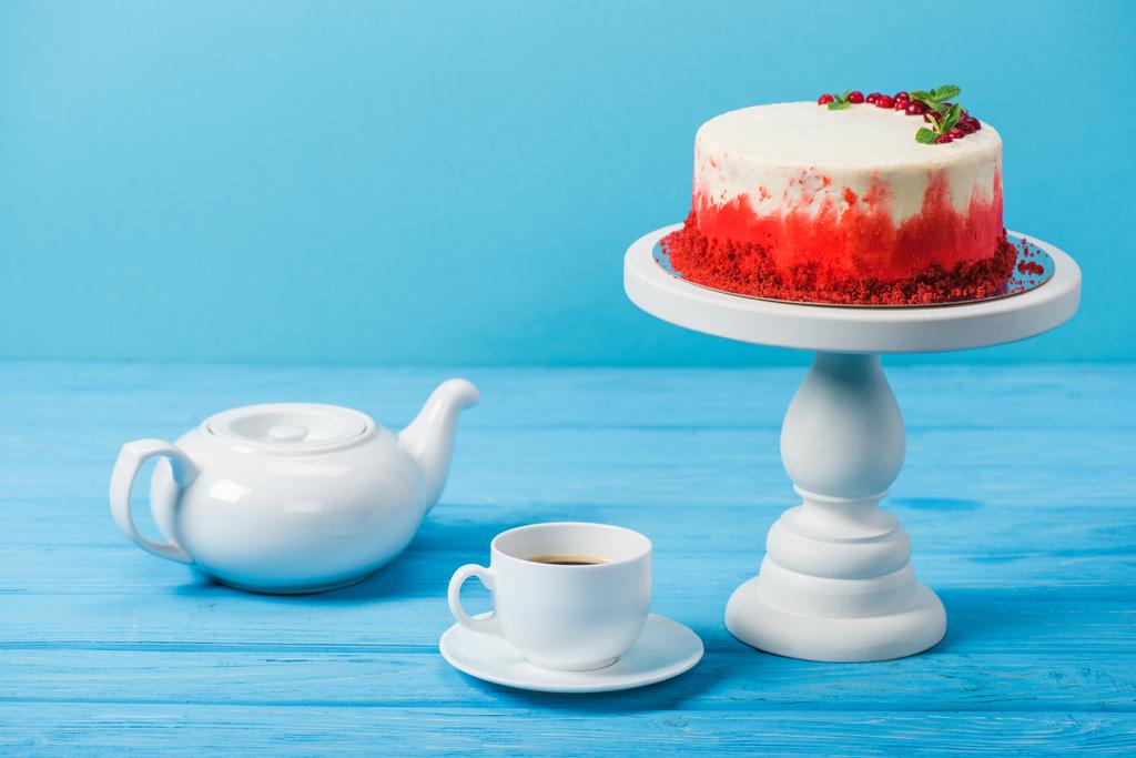 bolo decorado com groselhas vermelhas perto de xícara branca e pote de chá isolado em azul
 - Foto, Imagem