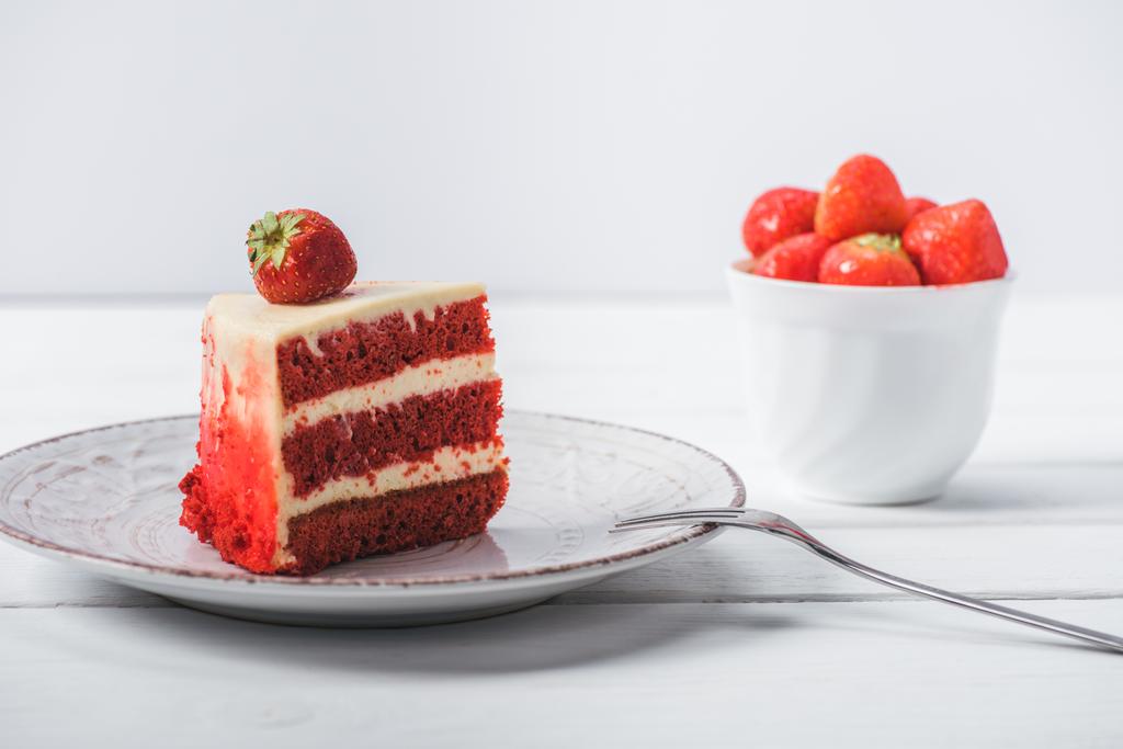 Stück roter Kuchen mit Erdbeere auf Untertasse in der Nähe Tasse mit Früchten isoliert auf weiß dekoriert  - Foto, Bild