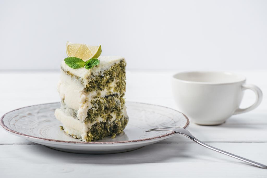 pedaço de bolo branco decorado com fatias de limão e folhas de hortelã no pires perto do copo isolado no branco
  - Foto, Imagem