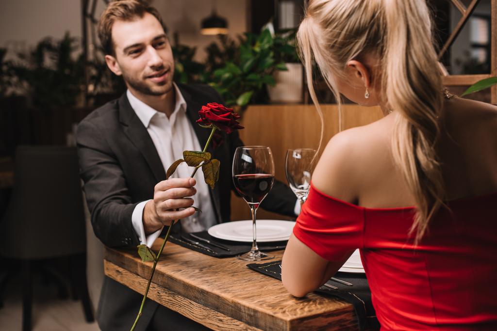 alegre hombre dando rojo rosa a novia mientras sentado en restaurante
  - Foto, imagen
