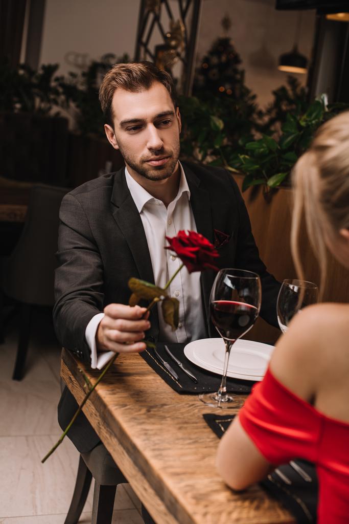 handsome man giving rose to girlfriend while sitting in restaurant  - Photo, Image
