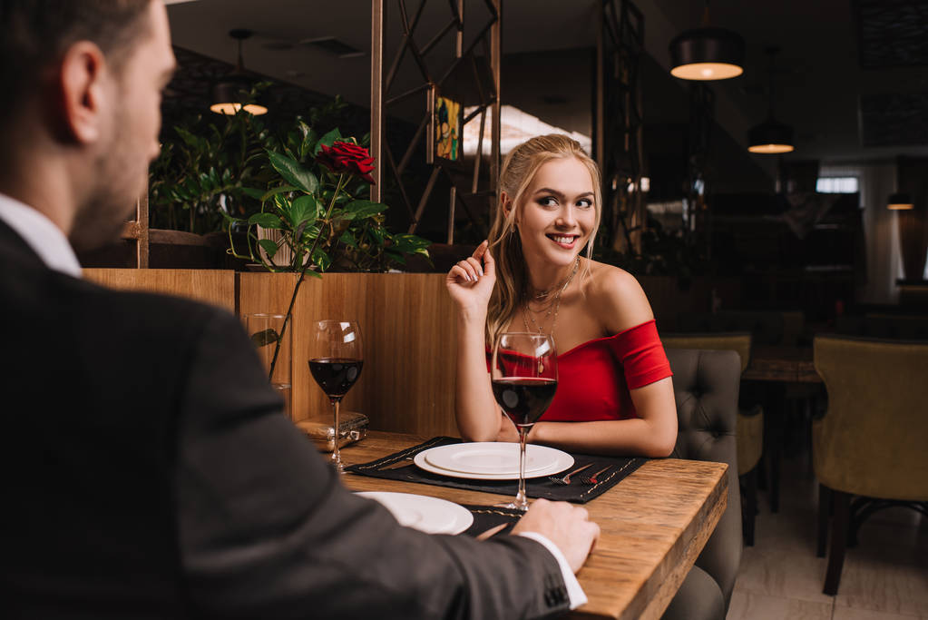 séduisante femme flirter avec petit ami tout en étant assis en robe rouge au restaurant
  - Photo, image