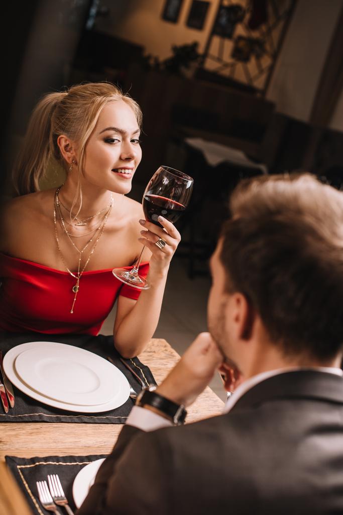 szelektív összpontosít, vonzó nő gazdaság üveg borral és flörtöl, miközben nézi az ember étteremben  - Fotó, kép