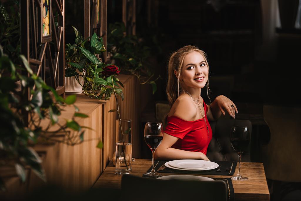 aantrekkelijke blonde vrouw in rode jurk in restaurant wachten  - Foto, afbeelding