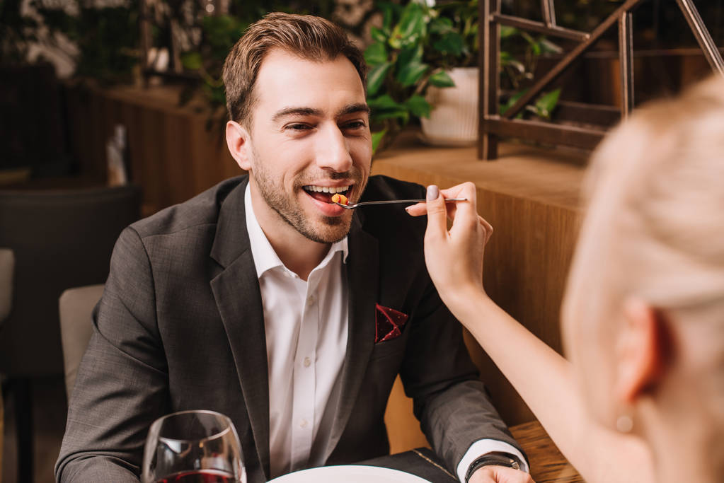 girlfriend feeding handsome man with sweet dessert in restaurant - Photo, Image