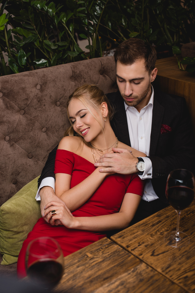 handsome man hugging attractive woman while sitting in restaurant  - Photo, Image