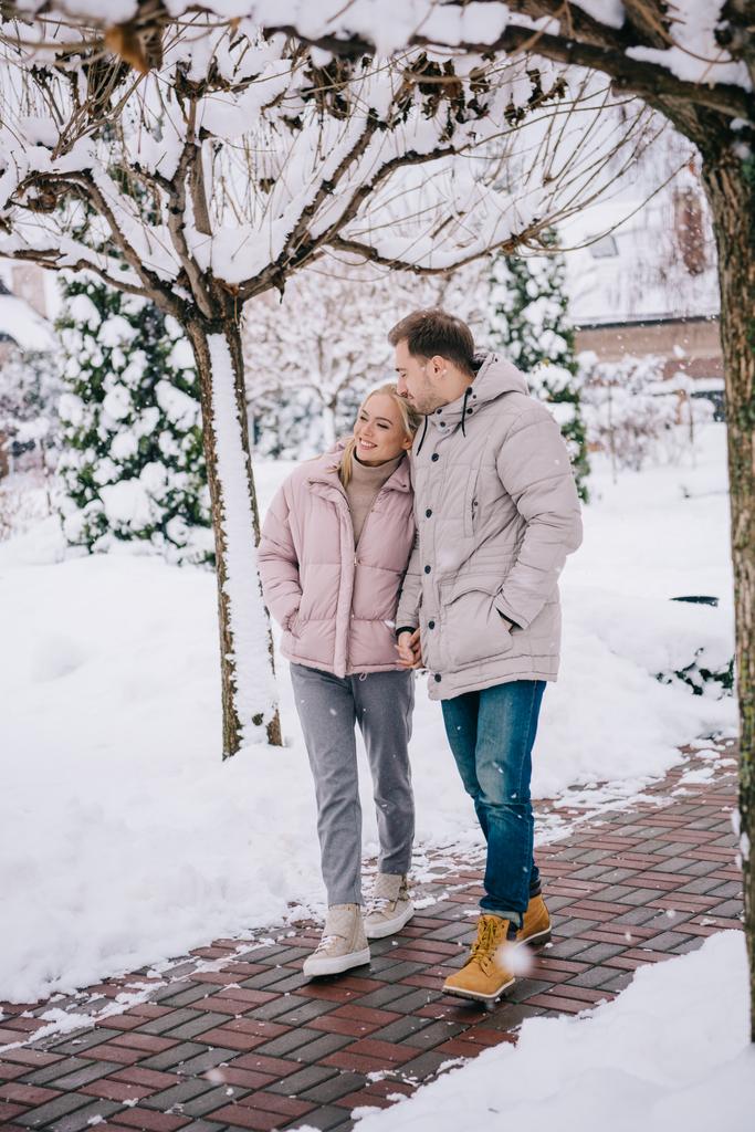 счастливые мужчина и женщина обнимаются и гуляют в зимнем парке
 - Фото, изображение