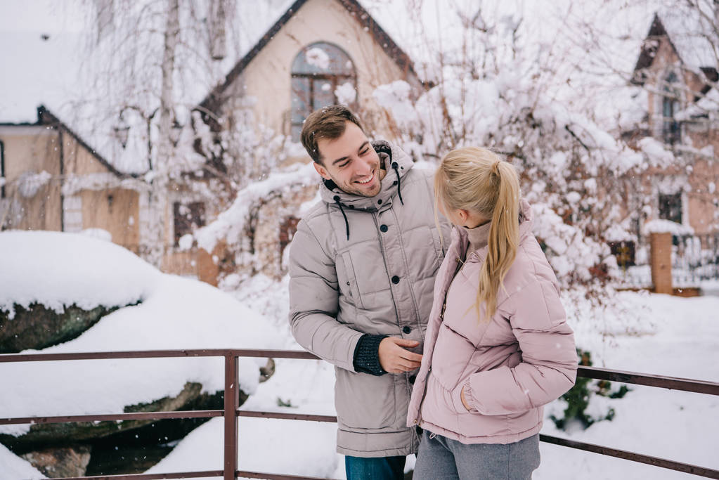 όμορφος άνδρας κοιτάζοντας ξανθιά κοπέλα και χαμογελώντας το χειμώνα  - Φωτογραφία, εικόνα