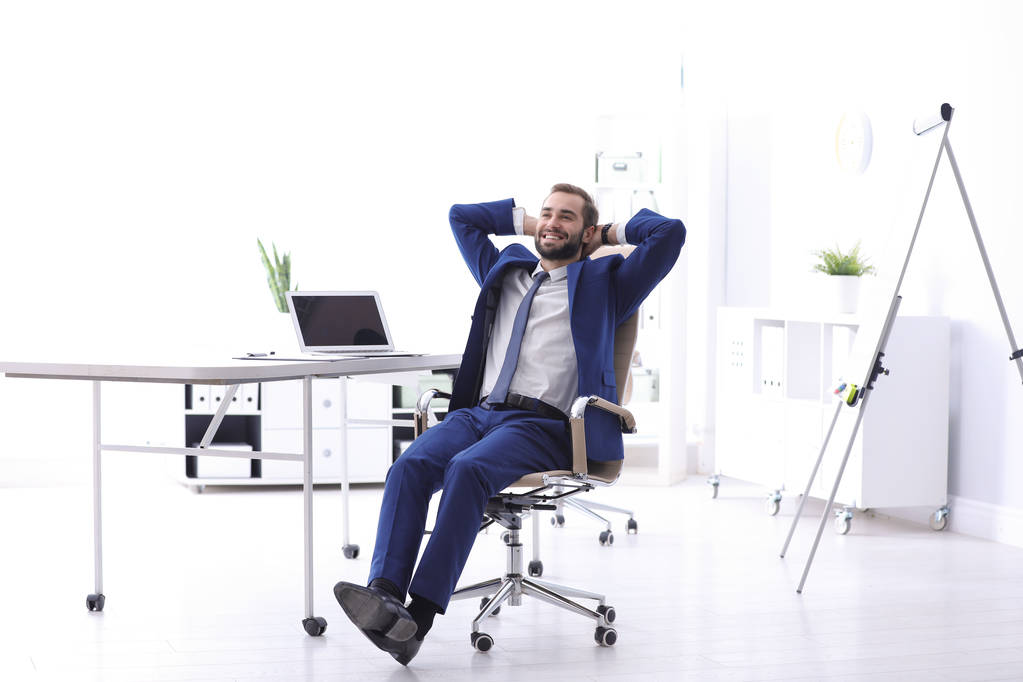 Νέος επιχειρηματίας που κάθεται στην καρέκλα του γραφείου άνετα στο χώρο εργασίας - Φωτογραφία, εικόνα