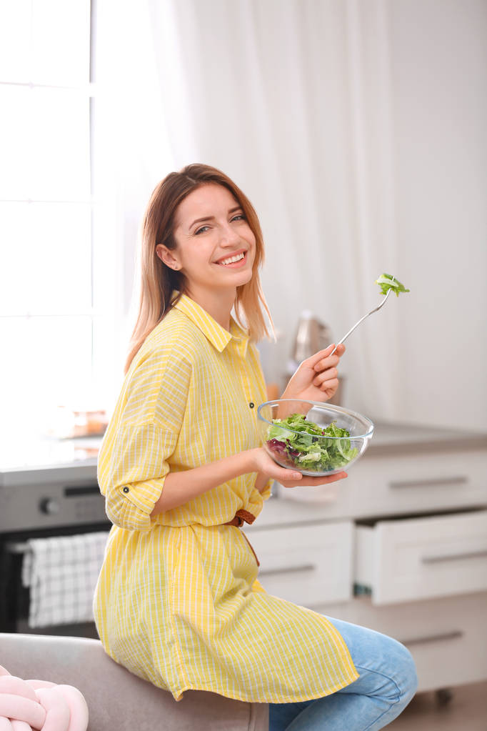 Jovem feliz comendo salada na cozinha. Dieta saudável
 - Foto, Imagem