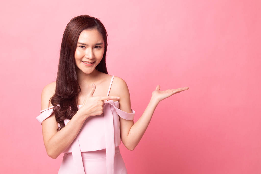 Hermosa mujer asiática joven punto a mano de palma sobre fondo rosa
 - Foto, imagen