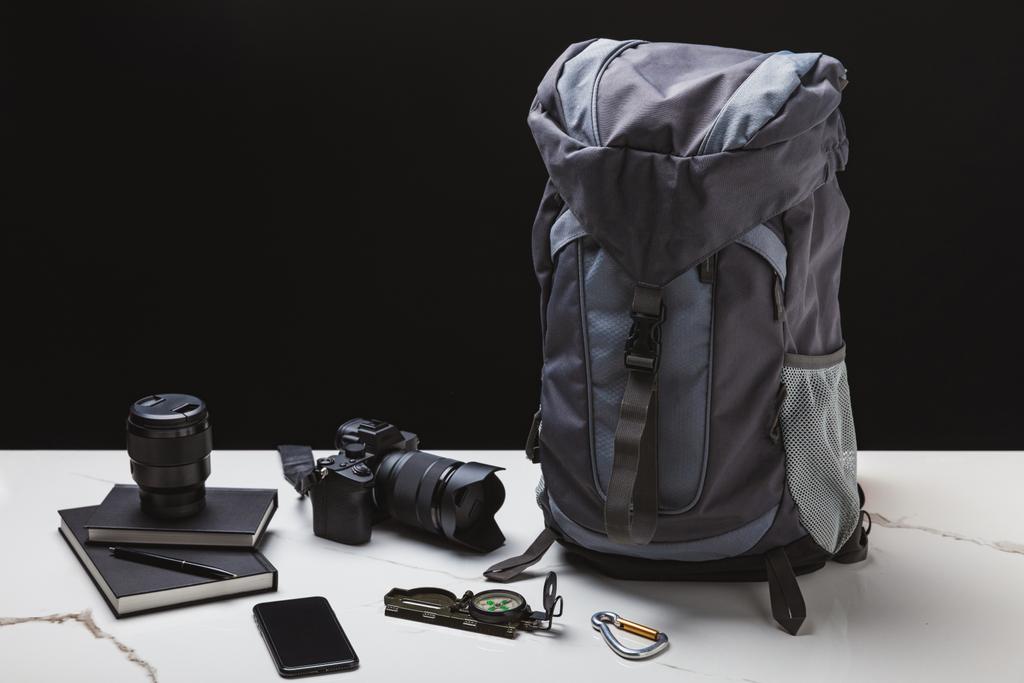 рюкзак, смартфон, компас, ноутбуки и фотокамера с объективом на черном
 - Фото, изображение