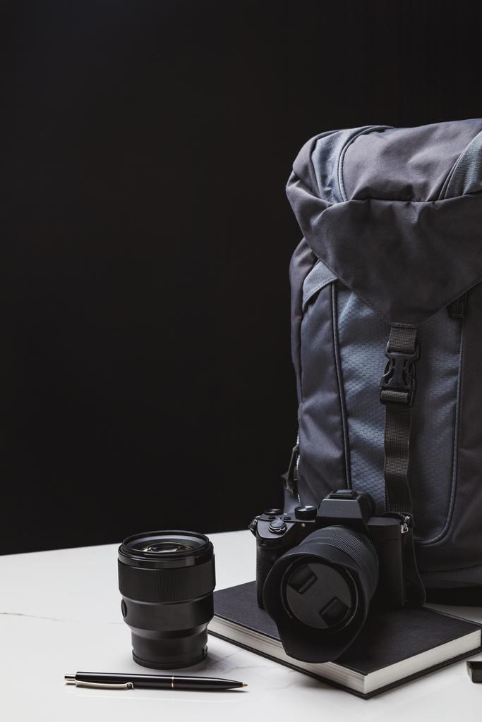 plecak, aparat fotograficzny z obiektywem i notebook z pióra na czarny  - Zdjęcie, obraz