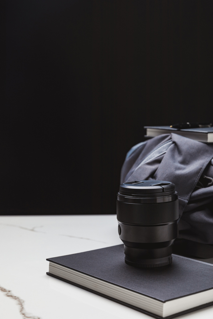close-up view of photo lens on notebook and backpack on black - Photo, Image