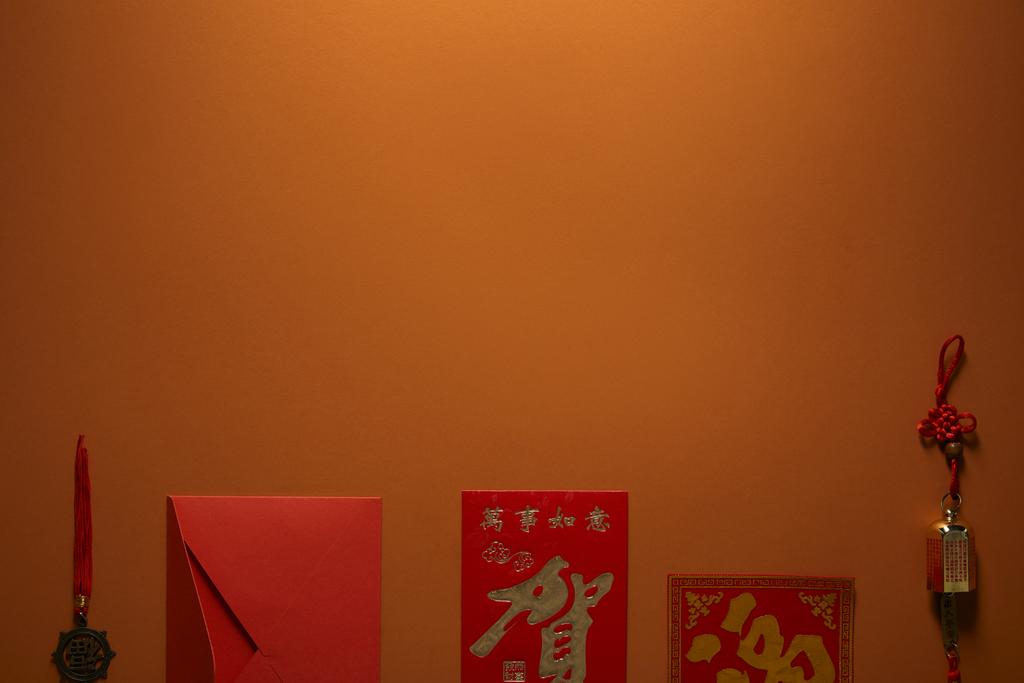 roter Umschlag, goldene chinesische Dekorationen und Hieroglyphen auf braunem Hintergrund - Foto, Bild
