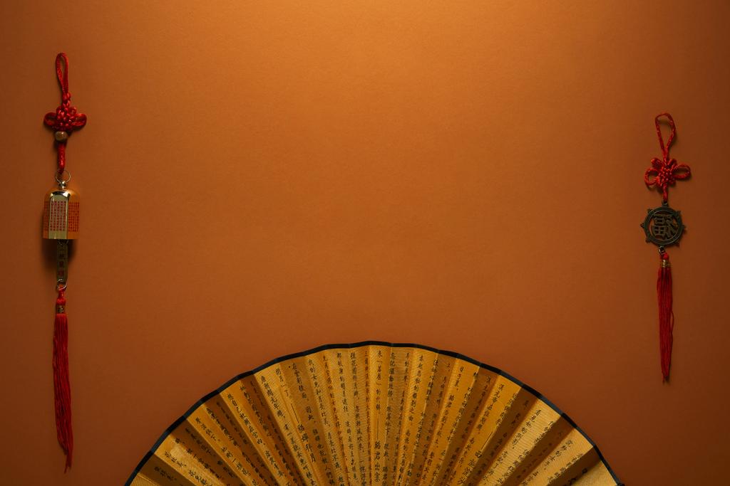 vista superior de abanico dorado con jeroglíficos y decoraciones chinas tradicionales sobre fondo marrón
 - Foto, Imagen