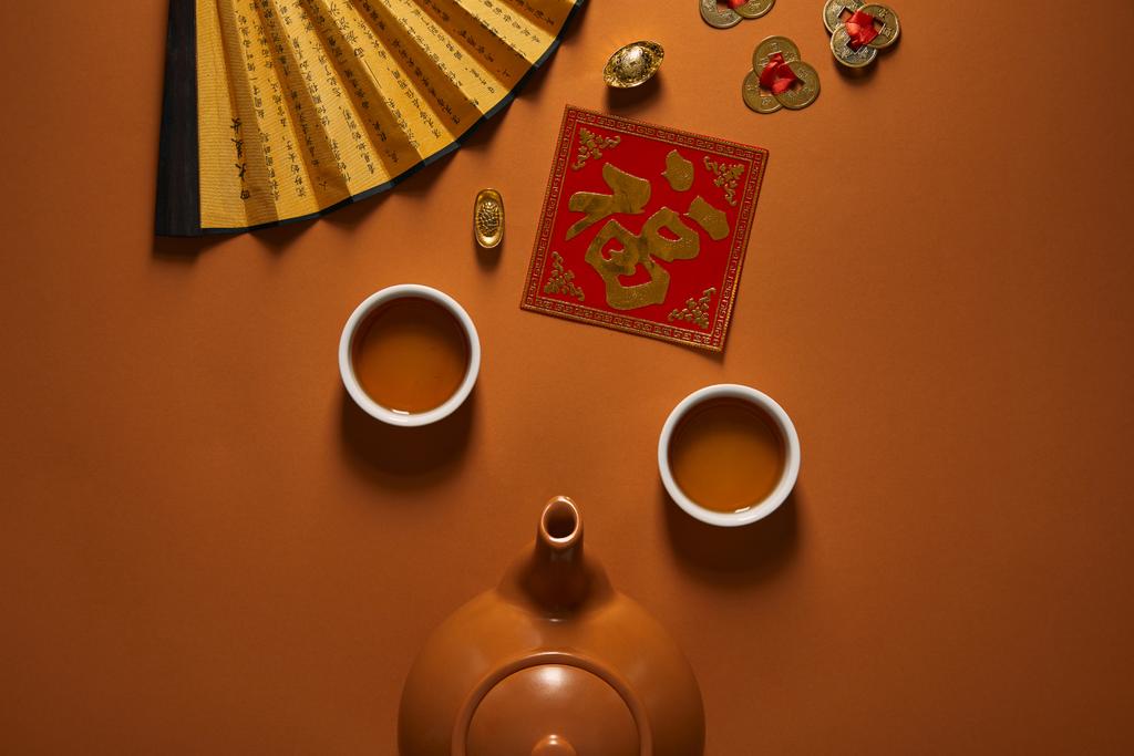 bovenaanzicht van thee set, ventilator met hiërogliefen en traditionele chinese decoraties op brown - Foto, afbeelding