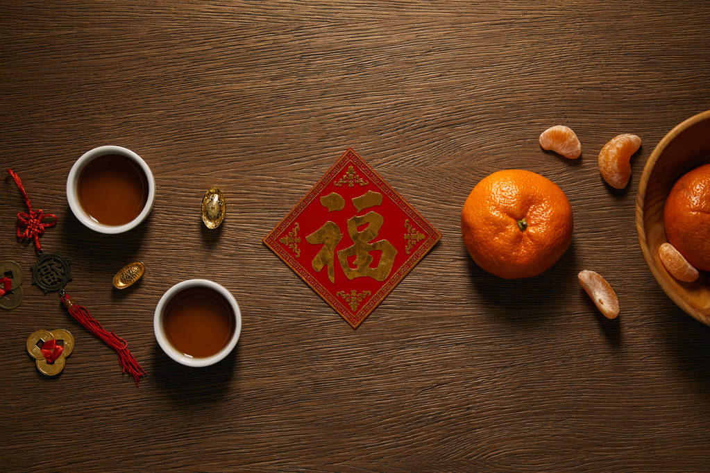 vista superior de mandarinas frescas maduras, jeroglífico dorado, tazas de té y monedas en la superficie de madera
  - Foto, Imagen