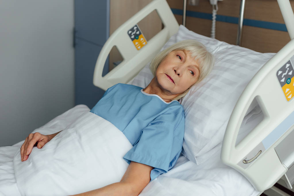 sad senior woman lying in bed in hospital and looking away - Photo, Image