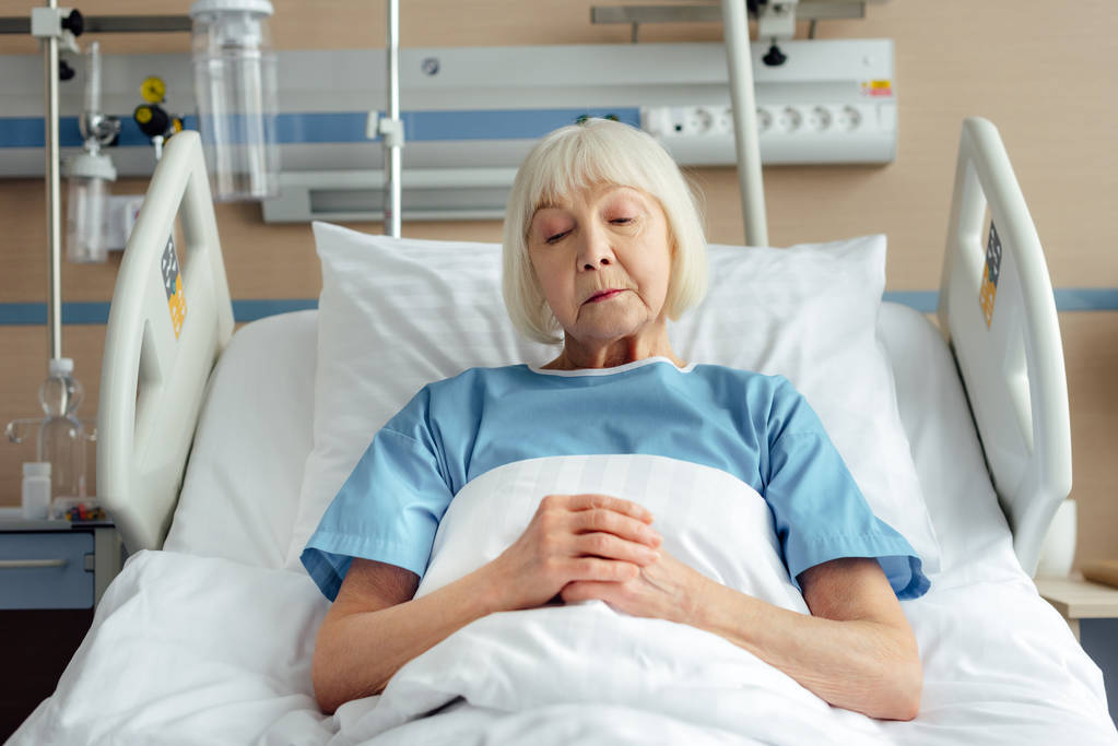 пожилая женщина со сложенными руками лежит в постели в больнице
  - Фото, изображение