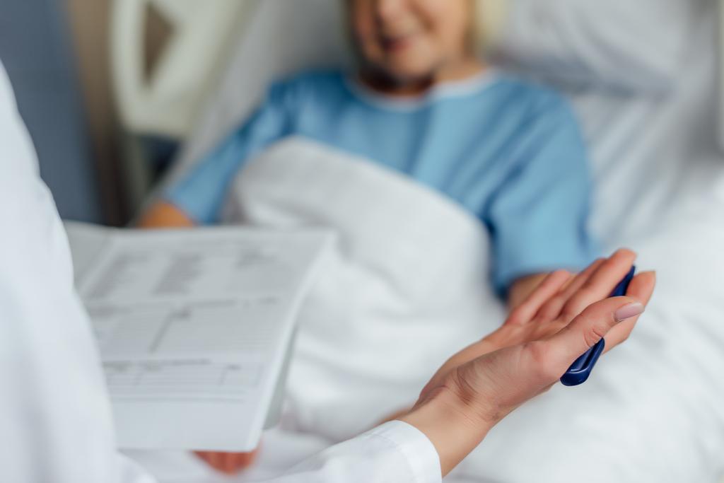 oříznutý pohled lékaře drží Diagnostika a poradenství, pacient leží v nemocniční posteli  - Fotografie, Obrázek