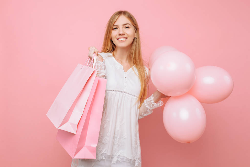 Happy young woman, in a white dress, with bags in hands and balloons, on a pink background - Photo, Image
