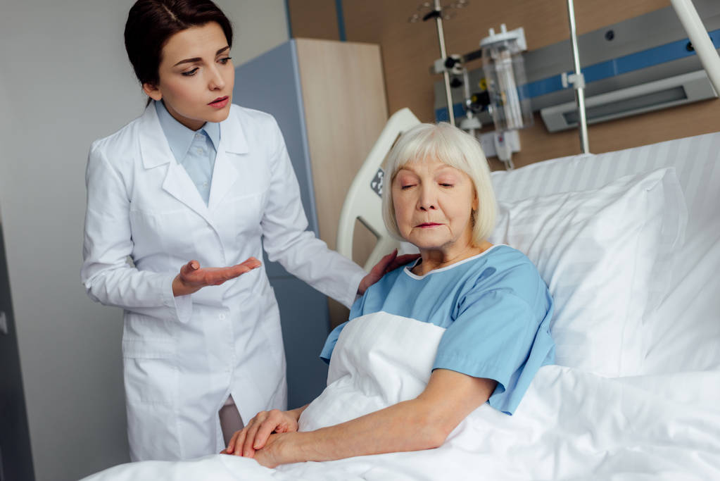 női orvos kézenfogva és tanácsadás ideges vezető nő a kórházi ágyon fekve - Fotó, kép