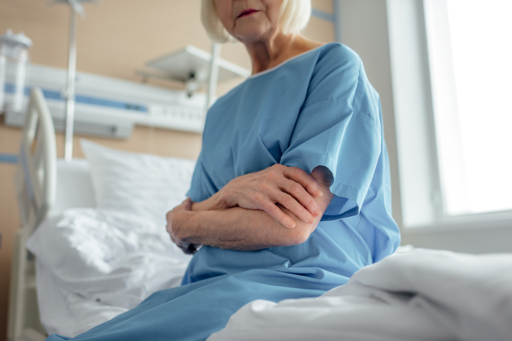 Ausgeschnittener Blick auf Seniorin mit verschränkten Armen, die auf Krankenhausstation im Bett sitzt  - Foto, Bild