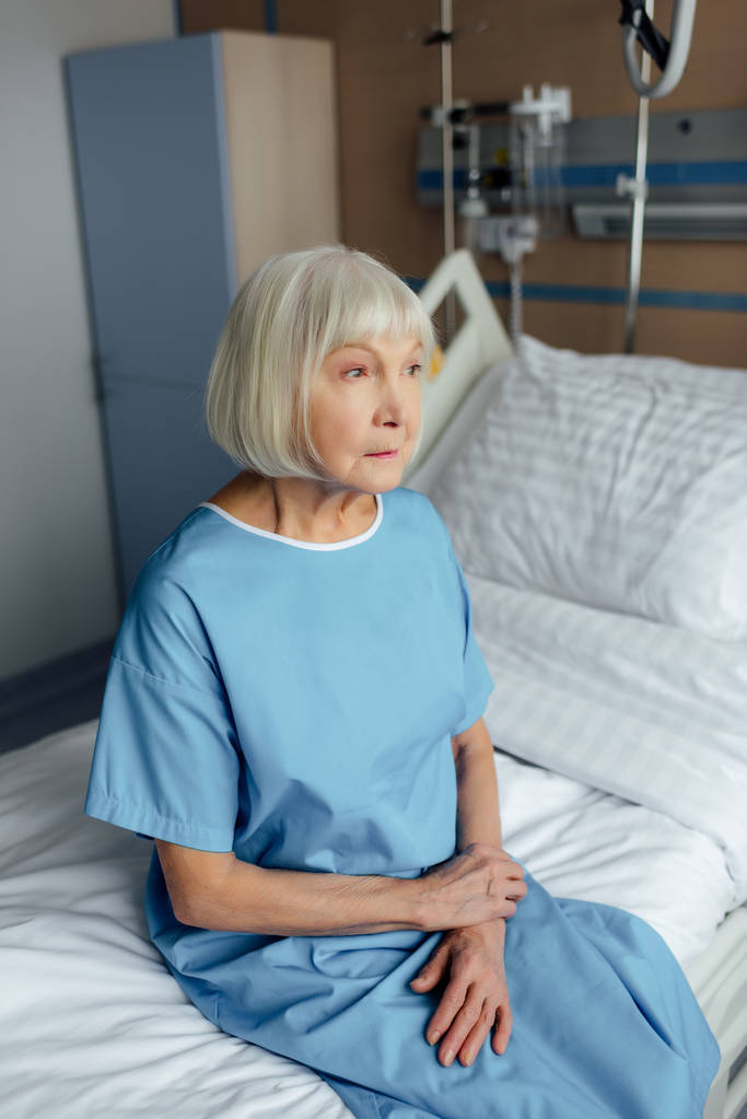 triste anciana con las manos dobladas sentada en la cama en el hospital
 - Foto, Imagen
