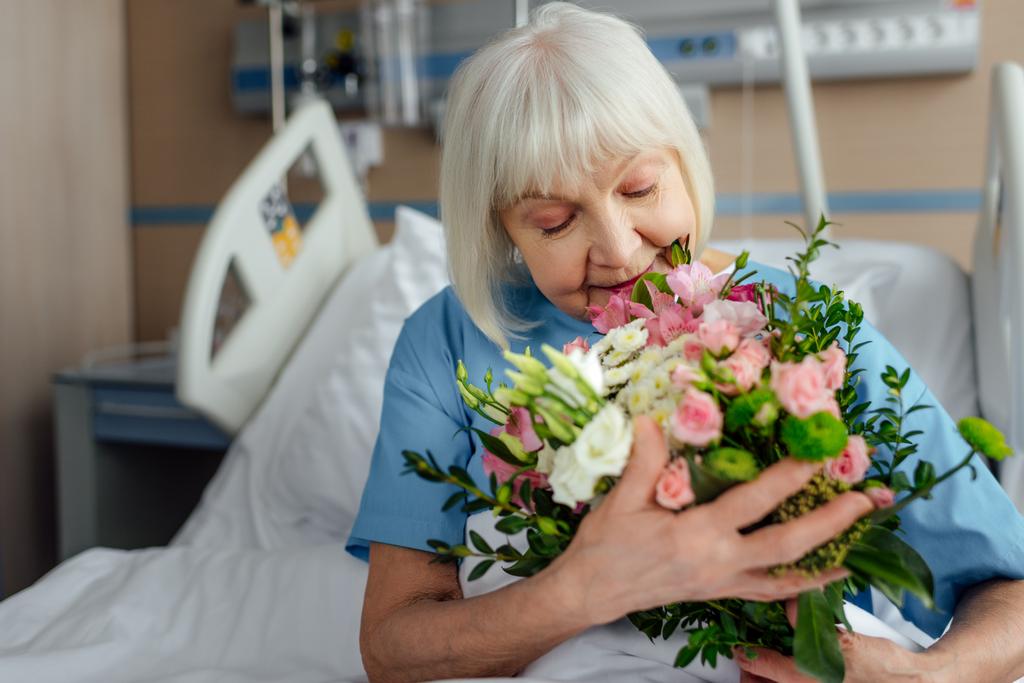 selective focus of recovering senior woman on bed with flowers in hospital - Photo, Image