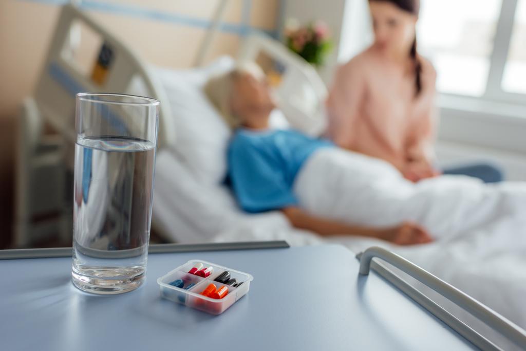 foco seletivo de vidro de água e medicina com paciente e visitante em segundo plano
 - Foto, Imagem