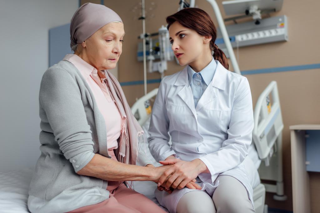 Besorgte Ärztin hält Hand in Hand mit krebskranker Seniorin im Krankenhaus - Foto, Bild