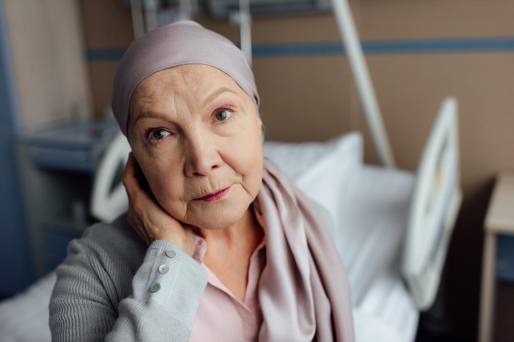 αναστατώσει ανώτερων γυναίκα με καρκίνο κάθεται στο κρεβάτι στο νοσοκομείο και να βλέπουν τα φωτογραφικών μηχανών - Φωτογραφία, εικόνα