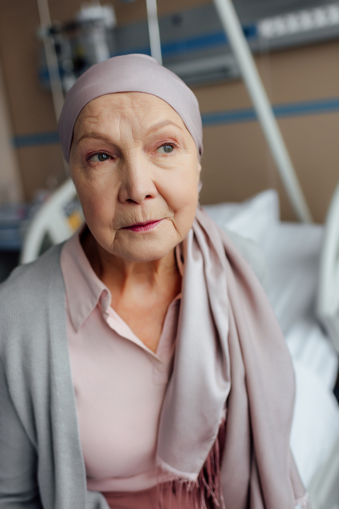 triest senior vrouw met kanker zittend op bed in het ziekenhuis en op zoek weg - Foto, afbeelding