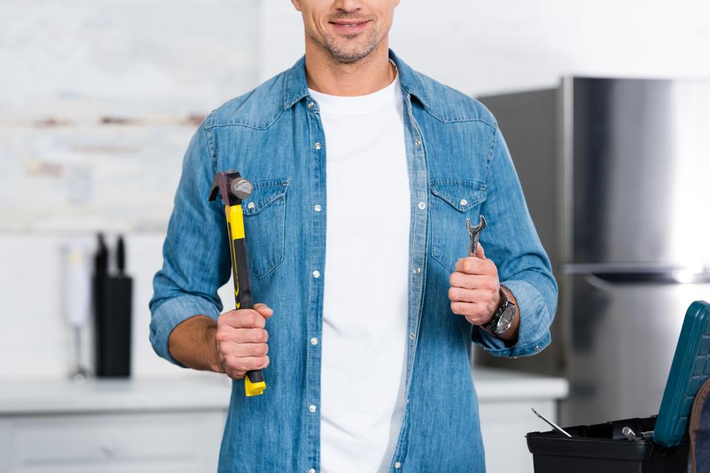 bijgesneden weergave van glimlachende man met hamer en sleutel in handen - Foto, afbeelding