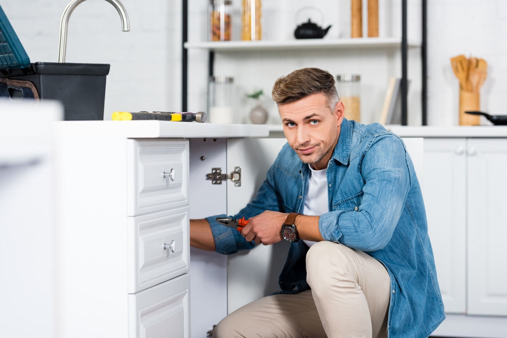 schöner Mann repariert Küchenspüle und schaut in die Kamera  - Foto, Bild