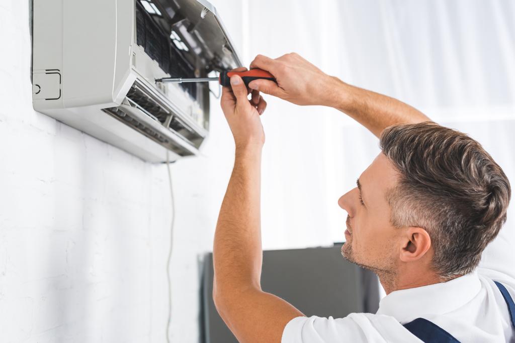 knappe volwassen man repareren airconditioner met schroevendraaier - Foto, afbeelding