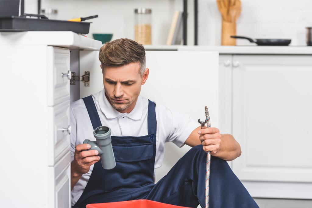 riparatore adulto premuroso seduto sotto il lavandino e tenendo i tubi per la riparazione in cucina
 - Foto, immagini