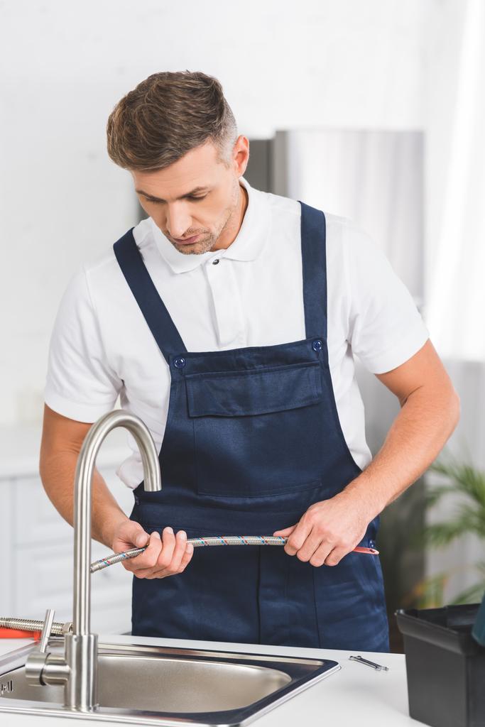 reparador adulto que sostiene la tubería mientras que repara el grifo en la cocina
  - Foto, Imagen